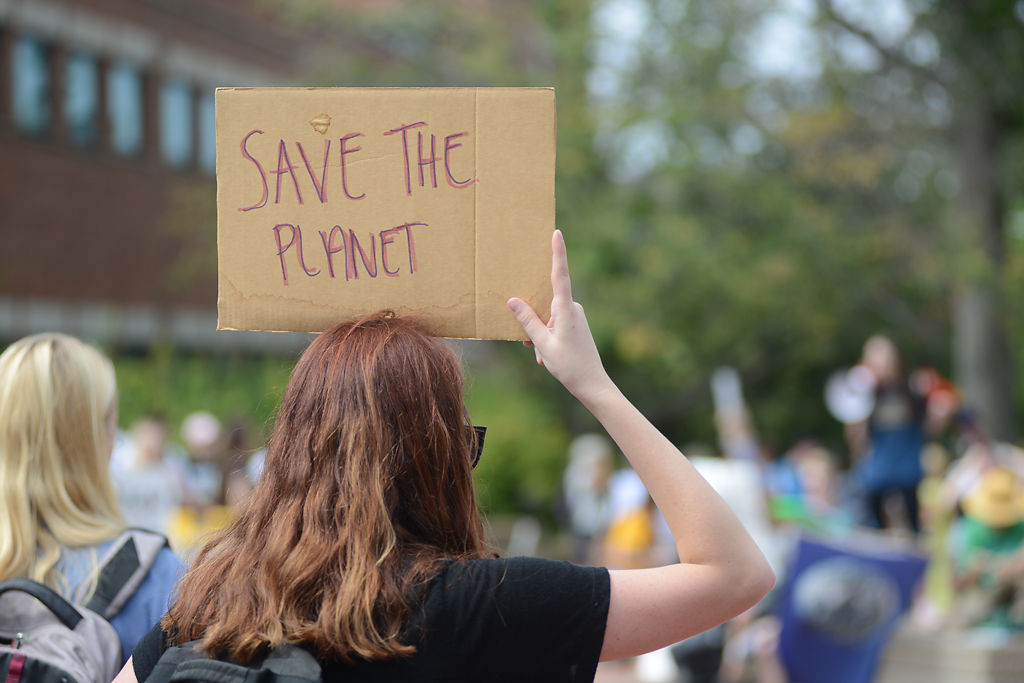 A protestor holds a sign at the Climate March as Barb Kuensting speaks to protestors on Friday